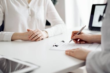 Doktor ve hasta klinikteki beyaz masada yan yana oturuyorlar. Kadın hekim bir kayıt formunu doldururken dinliyor. Tıp konsepti.