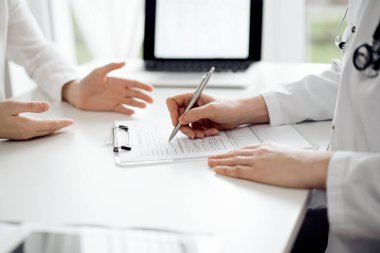 Doktor ve hasta klinikteki beyaz masada oturup bir şeyler tartışıyorlar. Kadın hekim bir kayıt formunu doldururken dinliyor. Tıp konsepti.