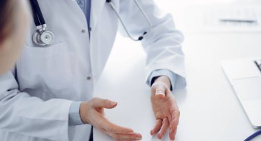Doktor ve hasta klinikteki masada otururken güncel sağlık sorularını tartışıyorlar, sadece eller kapalı. Tıp konsepti.
