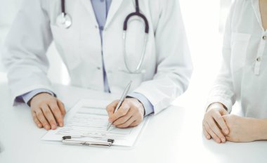 Doktor ve hasta klinikteki masada yan yana oturuyorlar. Kadın doktorların ellerinin tıbbi geçmiş kayıtlarını doldurması ya da kontrol listesi üzerinde yoğunlaşacağız. Kapat. Tıp konsepti.
