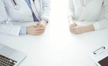 Doktor ve hasta klinikteki masada yan yana oturuyorlar, yakın plan. Tıp konsepti.