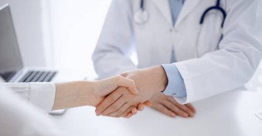 Klinikteki masada karşılıklı otururken doktor ve hasta el sıkışıyor. Sadece eller kapalı. Tıp konsepti.