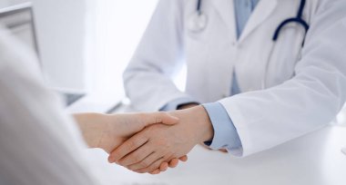 Klinikteki masada karşılıklı otururken doktor ve hasta el sıkışıyor. Sadece eller kapalı. Tıp konsepti.