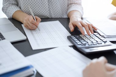 Müşteri ya da meslektaşıyla birlikte vergi sayarken hesap makinesi ve dizüstü bilgisayar kullanan kadın muhasebeci. İş denetleme ekibi, finans danışmanı.