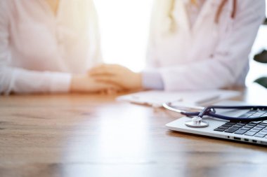 Stetoskop ve dizüstü bilgisayar ahşap masada yatarken doktorlar arka plandaki hastaya güvence veriyor. Tıp konsepti.