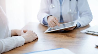 Doktor ve hasta klinikteki ahşap masada oturuyorlar. Dizüstü bilgisayar monitörüne bakan kadın doktorlar, kapatın. Tıp konsepti.