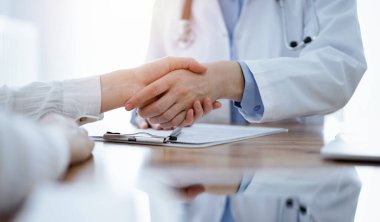 Doktor ve hasta klinikteki ahşap masanın üstünde el sıkışıyor. Tıp konsepti.