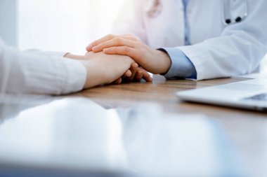 Doktor ve hasta klinikteki ahşap masada oturuyorlar. Kadın doktorların elleri güven veren kadınlarındır. Tıp konsepti.