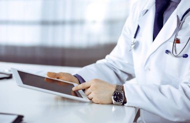 Bilinmeyen erkek doktor klinikteki tablet bilgisayarla yakın planda çalışıyor. İşteki genç doktor. Mükemmel sağlık hizmeti, tıp konsepti.