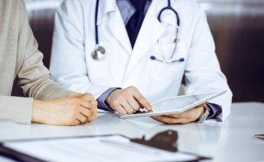 Bilinmeyen erkek doktor ve hasta kadın klinikte oturup tablet bilgisayar kullanırken bir şeyler tartışıyorlar. Hastanedeki en iyi sağlık hizmeti, ilaç, salgın durdurma..