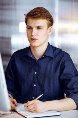 Genç sarışın işadamı karanlık bir ofiste bilgisayarla çalışıyor, arka planda ışık parıltısı var..