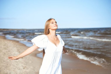 Mutlu gülümseyen güzel kadın okyanus sahilinde beyaz bir yaz elbisesi içinde, kolları açık..