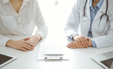 Doktor ve hasta birbirlerine yakın otururken sağlık sorularını tartışıyorlar ve klinikteki masada pano kullanıyorlar, sadece ellerini kapatıyorlar. Tıp konsepti.