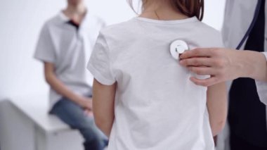 Doktor ve çocuk hasta klinikte. Beyaz önlüklü bir doktor steteskopla genç bir kızı muayene ediyor. İlaç, terapi konsepti.