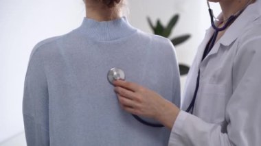 Doktor ve hasta klinikte. Beyaz önlüklü bir doktor steteskopla kadınları muayene ediyor. İlaç, terapi konsepti.