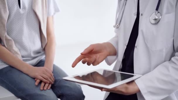 診療所で 医者と子供の患者が 向かい合って 小さな男の子の近くでタブレットコンピュータを使用する未知の女性医師 医学コンセプト — ストック動画