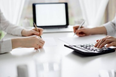 Ofisteki beyaz masada vergileri saymak için hesap makinesi ve dizüstü bilgisayar kullanan iki muhasebeci. İş denetimi ve finans alanında takım çalışması.