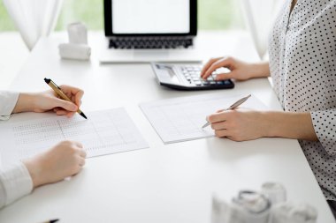 Hesap makinesi ve dizüstü bilgisayar kullanan iki muhasebeci vergileri ve gelir dengesini hesaplamak için beklerken makbuzlar da hesaplanmayı bekliyor. İş denetimi ve vergi kavramları.