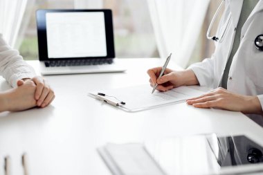 Doktor ve hasta klinikteki beyaz masada yan yana oturuyorlar. Kadın hekim bir kayıt formunu doldururken dinliyor. Tıp konsepti.