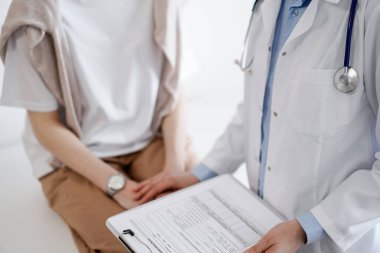 Doktor ve hasta sağlık muayenesi sonuçlarını tartışıyor. Dostane bir doktor, genç bir bayana bir yandan güvence verirken diğer yandan da tıbbi evraklarla pano tutuyor. Tıp konsepti.
