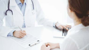 Doktor ve hasta bir şey tartışıyor ve klinikteki masada karşılıklı otururken dizüstü bilgisayar kullanıyorlar. Mükemmel tıbbi hizmet ve tıp konsepti.