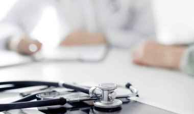Doktor ve hasta klinikteki masada oturmuş bir şey tartışıyorlar. Masada duran steteskopa odaklan, kapat. Mükemmel tıbbi hizmet ve tıp konsepti.