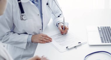 Doktor ve hasta klinikteki masada oturuyor. Kadın doktorların ellerinin tıbbi geçmiş kayıtlarını doldurması ya da kontrol listesi üzerinde yoğunlaşacağız. Kapat. Tıp konsepti.