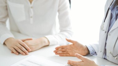 Doktor ve hasta birbirlerine yakın otururken sağlık sorularını tartışıyorlar ve klinikteki masada pano kullanıyorlar, sadece ellerini kapatıyorlar. Tıp konsepti.