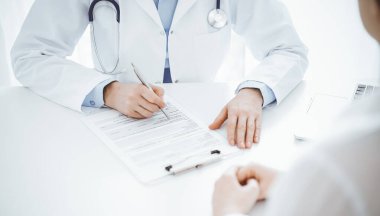 Doktor ve hasta, klinikteki masada karşılıklı otururken mevcut sağlık sorunlarını tartışıyorlar. Sadece ellerinizi yakın plan yapın. Tıp konsepti.