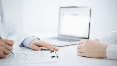 Doktor ve hasta klinikteki masada karşılıklı oturuyorlar. Kadın doktorların ellerinin tıbbi geçmiş kayıtlarını doldurması ya da kontrol listesi üzerinde yoğunlaşacağız. Kapat. Tıp konsepti.