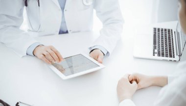 Doktor ve hasta klinikteki masada karşılıklı oturuyorlar. Kadın doktorların elleri tablet bilgisayarın dokunmatik dokunmatik pedini işaret ediyor, kapat. Tıp konsepti.