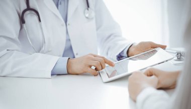 Doktor ve hasta klinikteki masada karşılıklı oturuyorlar. Kadın doktorların elleri tablet bilgisayarın dokunmatik dokunmatik pedini işaret ediyor, kapat. Tıp konsepti.