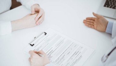 Doktor ve hasta birbirlerine karşı otururken sağlık sorularını tartışıyorlar ve klinikteki masada pano kullanıyorlar, sadece elleri yakın çekim. Tıp konsepti.