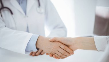 Klinikteki masada karşılıklı otururken doktor ve hasta el sıkışıyor. Sadece eller kapalı. Tıp konsepti.