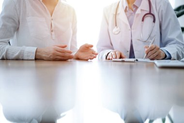 Doktor ve hasta klinikteki ahşap masada yan yana oturuyorlar. Kadın doktorlar kayıt formunu dolduruyorlar. Tıp konsepti.