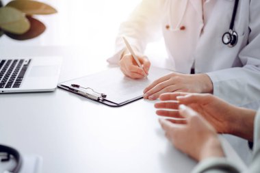 Doktor ve hasta klinikteki masada oturuyorlar. Kadın doktorların ellerinin ilaç geçmişi formunu doldurmasına odaklan, kapat. Tıp konsepti.