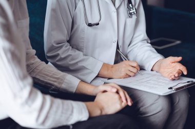 Doktor ve hasta klinikteki koltukta oturuyor. Kadın doktorların ellerinin ilaç geçmişi formunu doldurmasına odaklan, kapat. Tıp konsepti.