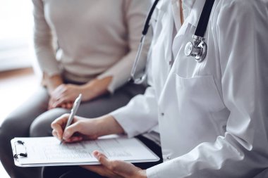 Doktor ve hasta klinikteki koltukta oturuyor. Kadın doktorların ellerinin ilaç geçmişi formunu doldurmasına odaklan, kapat. Tıp konsepti.