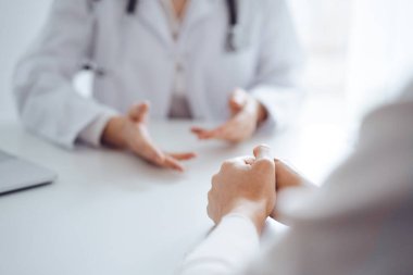 Doktor ve hasta klinikteki masada otururken sağlık muayenesini tartışıyorlar. Kadın hastaların ellerine odaklan, kapat. Tıp konsepti.