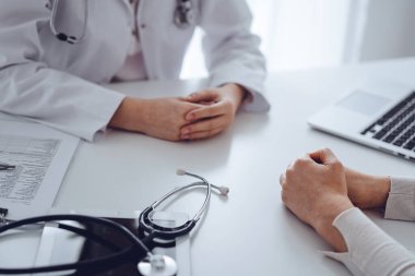 Doktor ve hasta klinikteki masada oturup bir şey tartışıyorlar. Masada duran steteskopa odaklan, kapat. Tıp ve sağlık hizmetleri kavramı.