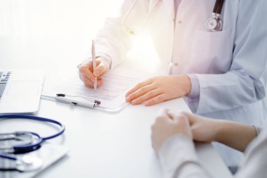 Doktor ve hasta klinikteki masada oturuyor. Kadın doktorların ellerinin tıbbi geçmiş kayıtlarını doldurması ya da kontrol listesi üzerinde yoğunlaşacağız. Kapat. Tıp konsepti.