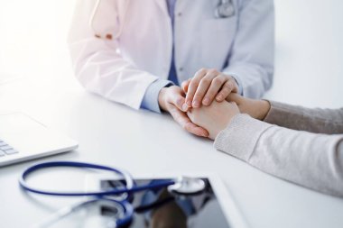 Doktor ve hasta klinikteki masada oturuyor. Kadın hekimlere odaklanıyor. Kadını rahatlatan eller. Sadece eller kapalı. Tıp konsepti.