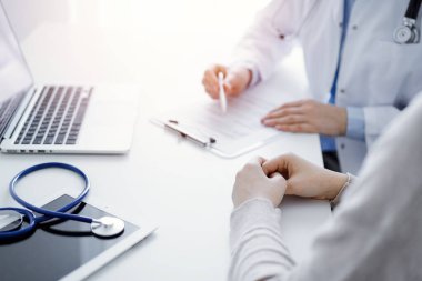 Doktor ve hasta klinikteki masada oturuyor. Kadın doktorların ellerinin tıbbi geçmiş kayıtlarını doldurması ya da kontrol listesi üzerinde yoğunlaşacağız. Kapat. Tıp konsepti.