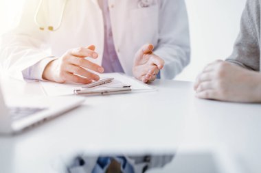 Doktor ve hasta klinikteki masada otururken güncel sağlık sorularını tartışıyorlar, sadece eller kapalı. Tıp konsepti.