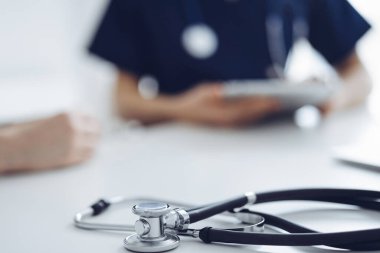 Steteskop arka planda bir doktor ve hastanın önünde tablet bilgisayarın üzerinde duruyordu. Tıp, sağlık hizmeti kavramı.