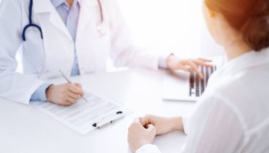 Doktor ve hasta bir şey tartışıyor ve klinikteki masada karşılıklı otururken dizüstü bilgisayar kullanıyorlar. Mükemmel tıbbi hizmet ve tıp konsepti.