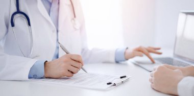 Doktor ve hasta bir şey tartışıyor ve klinikteki masada karşılıklı otururken dizüstü bilgisayar kullanıyorlar. Mükemmel tıbbi hizmet ve tıp konsepti.