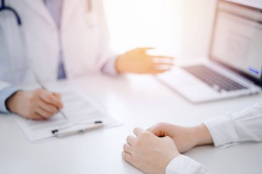 Doktor ve hasta klinikteki masada karşılıklı otururken tablet bilgisayar kullanıyorlar. Doktorun yanındaki kadın ellerine odaklan, yakın çekim. Tıp konsepti.