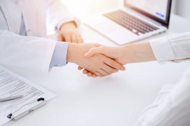 Klinikteki masada karşılıklı otururken doktor ve hasta el sıkışıyor. Sadece eller kapalı. Tıp konsepti.