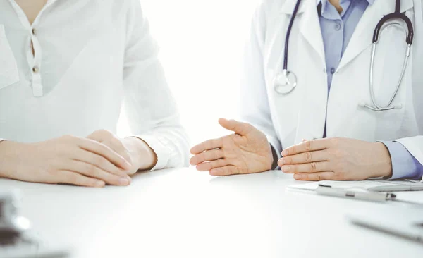 Doctor and patient discussing current health questions while sitting near of each other at the table in clinic, just hands closeup. Medicine concept.